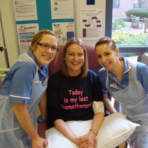 Servicer user Kathryn on her final day of chemo sitting in a chair with two nurses by her side