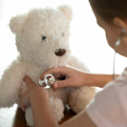 Close up of caring small girl child use stethoscope examine sick teddy bear play hospital or clinic. Little kid hold phonendoscope listen to toy animal heart lungs. Medicine, healthcare concept.