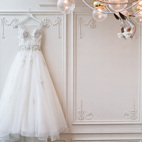 A bridal dress hung up on against a delicately decorated wall.