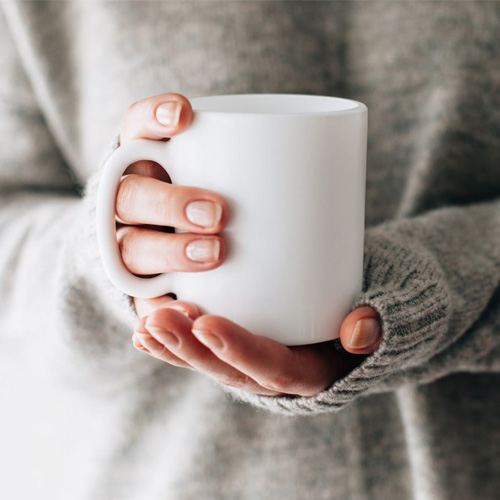 A picture of somebody holding a drink in a white mug.