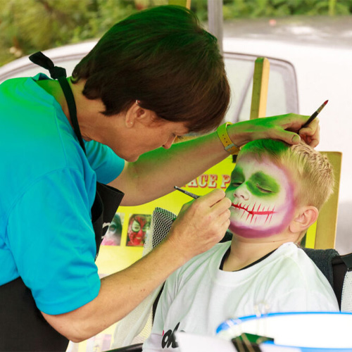 A woman painting on the face of a young boy.