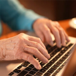 A close up of an older lady, typing on a laptop keyboard.