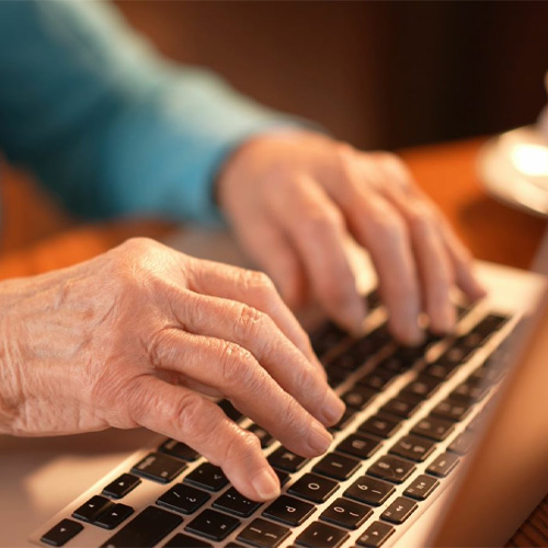 A close up of an older lady, typing on a laptop keyboard.
