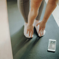 A woman stretching, touching her toes whilst listening to a fitness podcast.