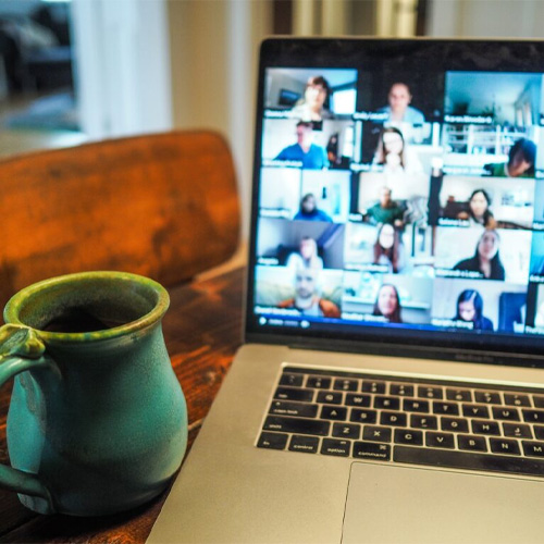 A picture of a green mug with a laptop meeting in the background.