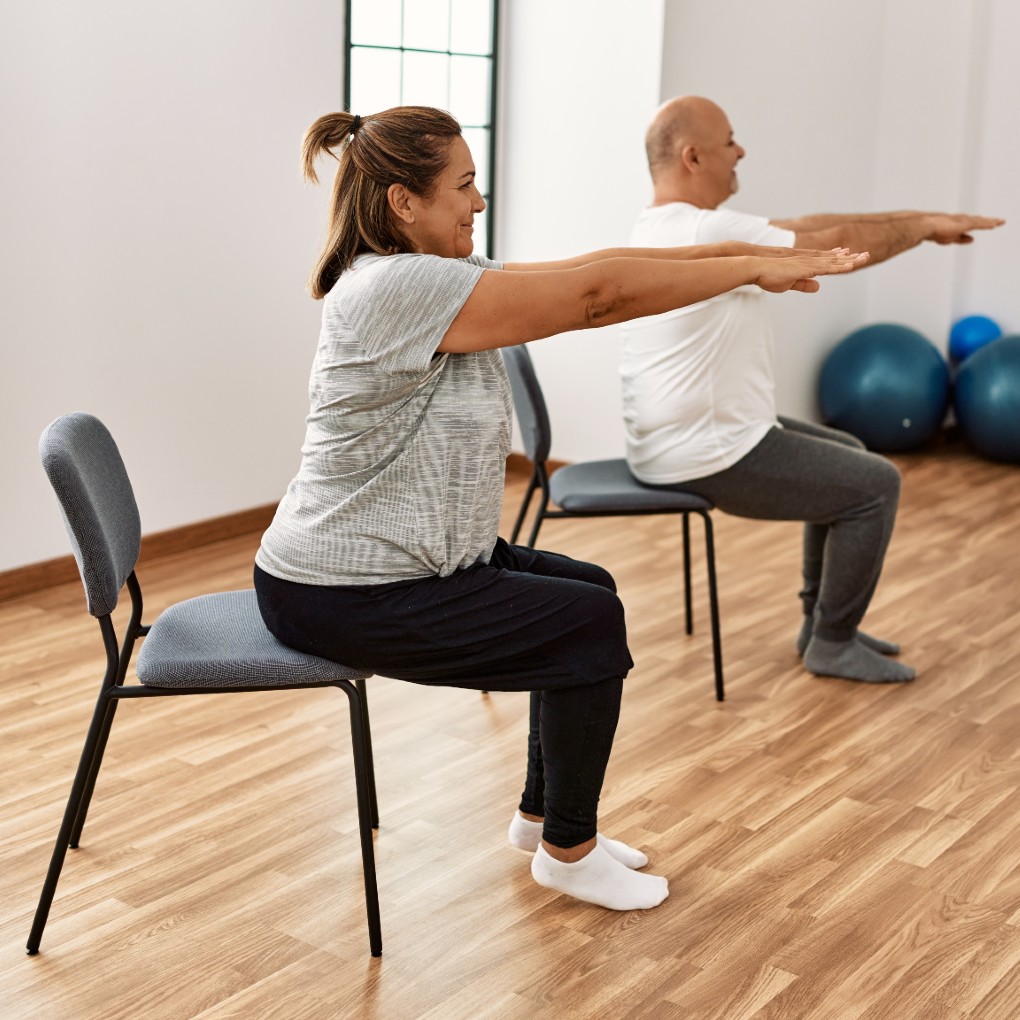 A man and a woman doing chair yoga in a fitness studio