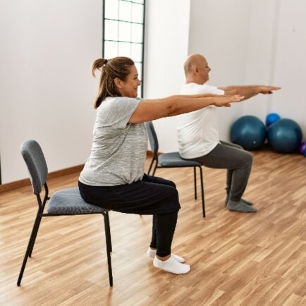 Two people doing a seated pilates class with their arms out in front of them