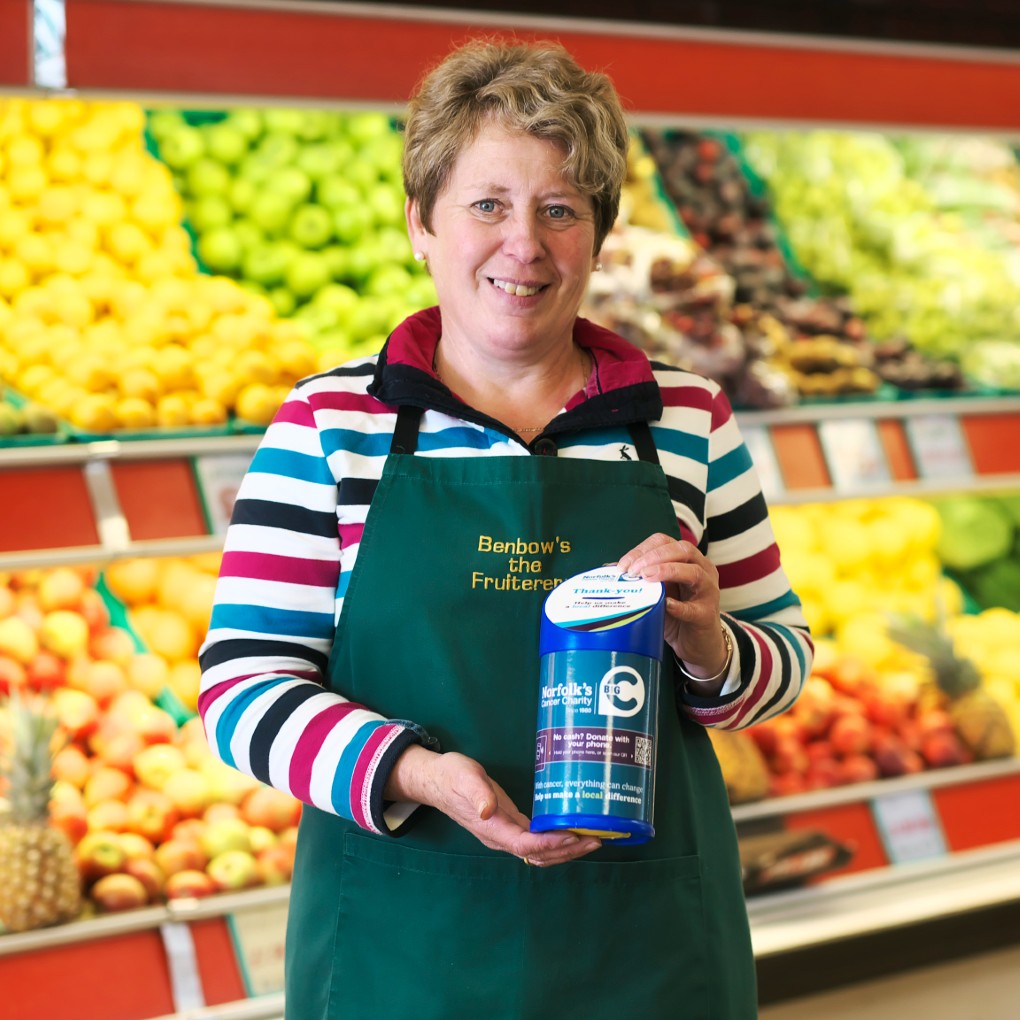 A lady on a greengrocers shop holding a donation tin for Big C.