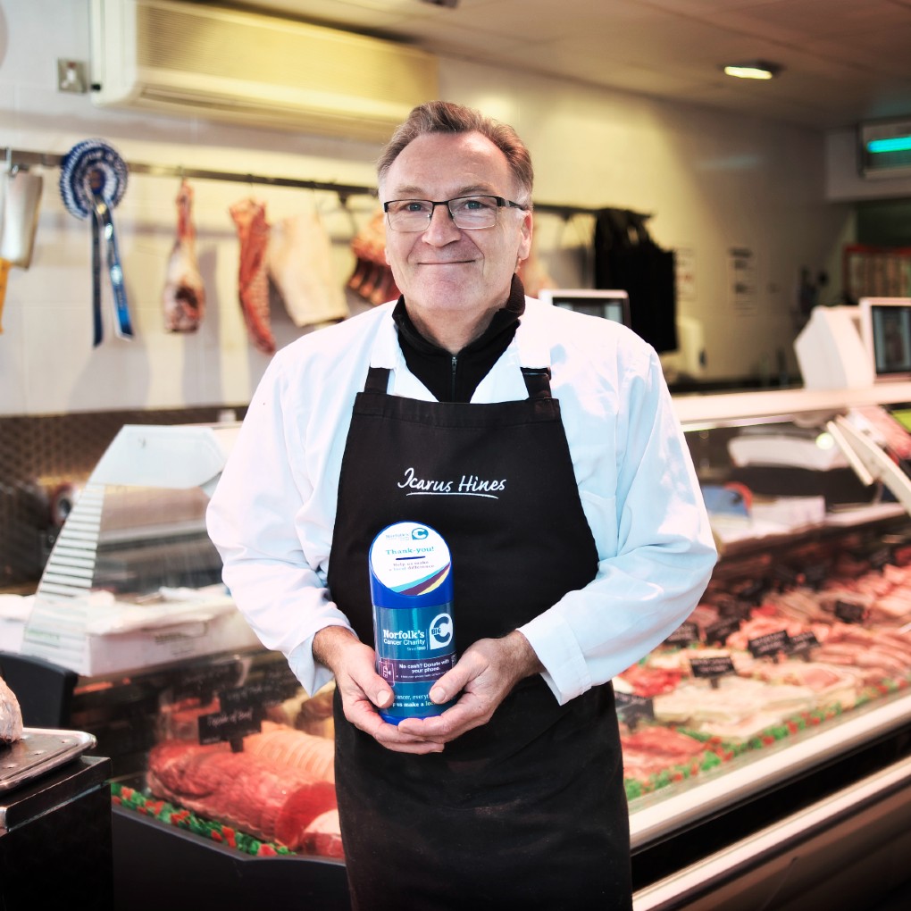 A man in a butchers shop holding a donation tin for Big C