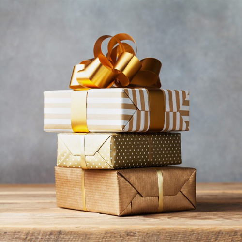 A stack of 3 presents, wrapped in gold and white wrapping paper and a large gold ribbon on top