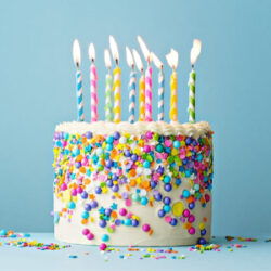 A birthday cake covered in multicoloured sprinkles and 10 candles