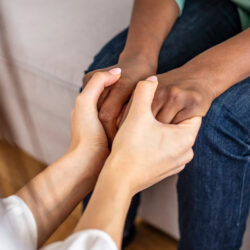 A close up of a person comforting another by holding their hands