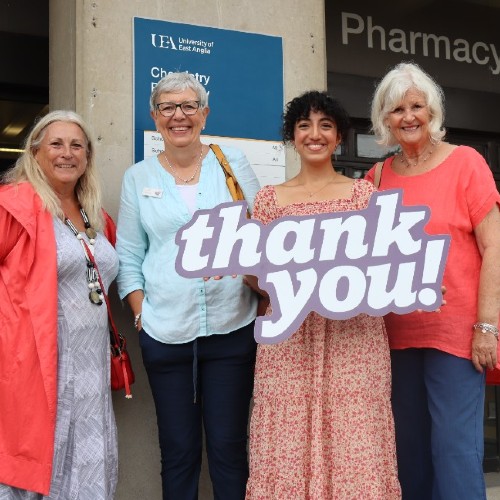 Student Rana standing holding a thank you board surrounded by three of the LILAC ladies fundraising group