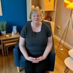 An image of one of our complementary therapists, Margaret sitting in a chair.