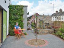 A pation garden at the Norwich City Support Centre, with a table and chairs and people outside enjoying the garden
