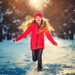 Girl running in a snowy forest wearing a red jacket, having fun