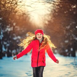 Girl running in a snowy forest with a red jacket on, smiling and having fun