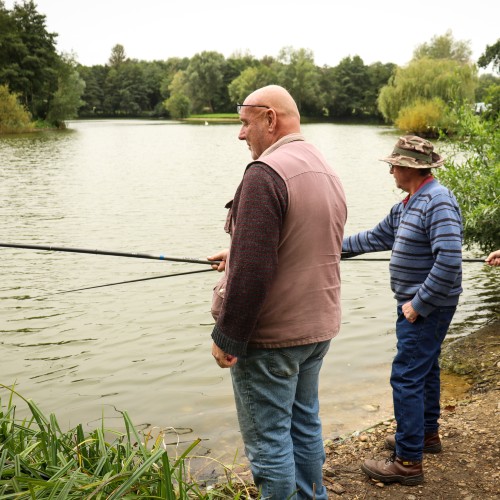 Two people fishing, standing by a lake
