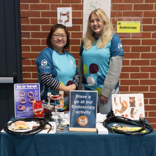 Two members of staff from the Endoscopy team at the Norfolk and Norwich Hospital standing by a table of activities